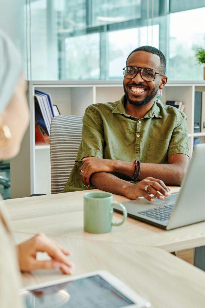 Cheerful man working at a desk in a modern office with laptop and coffee mug.